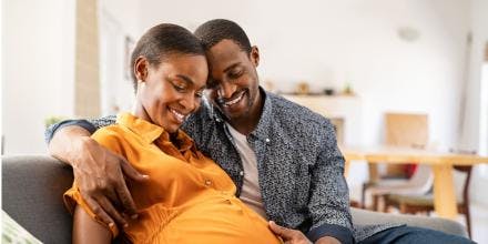 Black expectant parents sitting on sofa dreaming about their baby